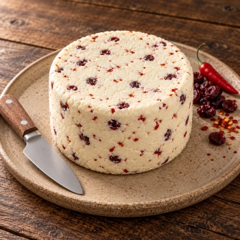 Niewędzony ser z chilli i żurawiną 1,5 kg na ceramicznym talerzu z papryczką, żurawiną i nożem.